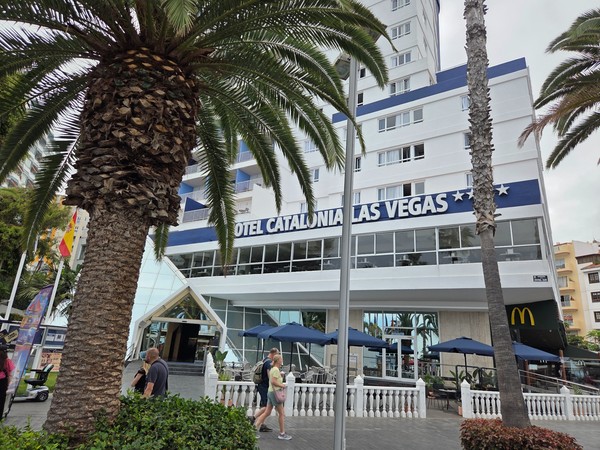 Fachada del Hotel Catalonia Las Vegas en Puerto de la Cruz, con palmeras, terraza exterior y peatones caminando frente a la entrada principal.