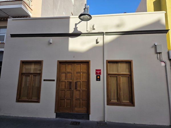 Fachada de El Taller Seve Díaz en Puerto de la Cruz, con paredes claras, puerta y ventanas de madera y placa distintiva en la entrada.