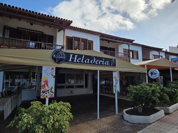 Heladería en Puerto de la Cruz con toldo beige, cartel principal y terrazas cubiertas en un entorno urbano con arquitectura tradicional.