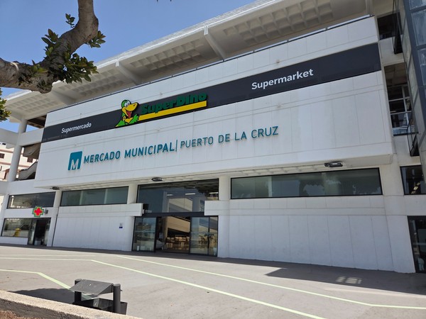 Fachada moderna del Mercado Municipal de Puerto de la Cruz con el supermercado SuperDino en la planta superior y una entrada amplia al mercado.