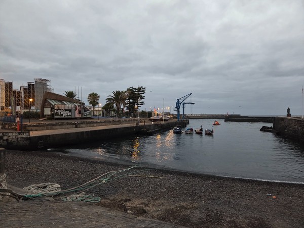 Vista del muelle del Puerto de la Cruz al atardecer con barcas y reflejos de las luces en el agua.