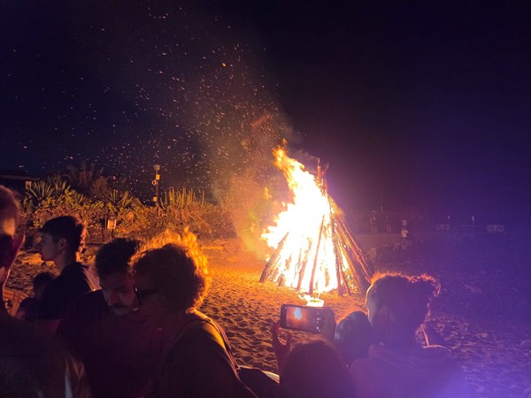 Hoguera de la Noche de San Juan en la playa con personas alrededor disfrutando de la fiesta.