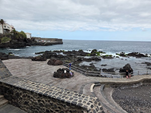 Piscinas naturales de San Telmo en Puerto de la Cruz, con plataformas de piedra volcánica, rocas negras y el océano Atlántico en marea tranquila.