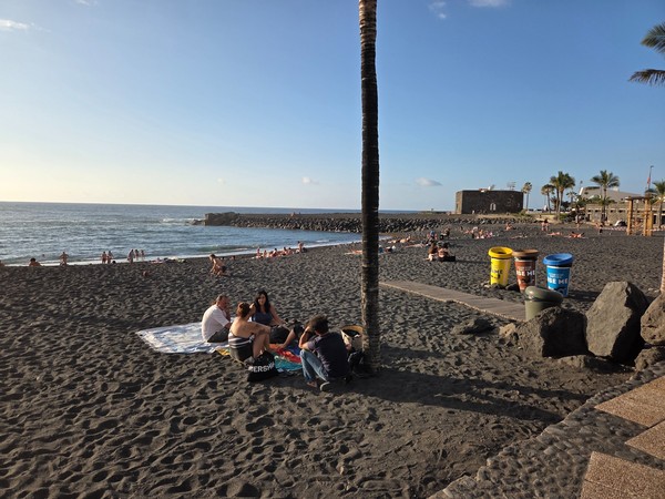 Playa Jardín en Puerto de la Cruz al atardecer con arena negra, palmeras y vistas al Castillo de San Felipe.