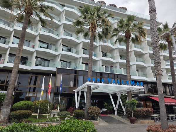 Entrada del Hotel Vallemar en Puerto de la Cruz, con su moderno edificio blanco, balcones acristalados y banderas ondeando frente al jardín.